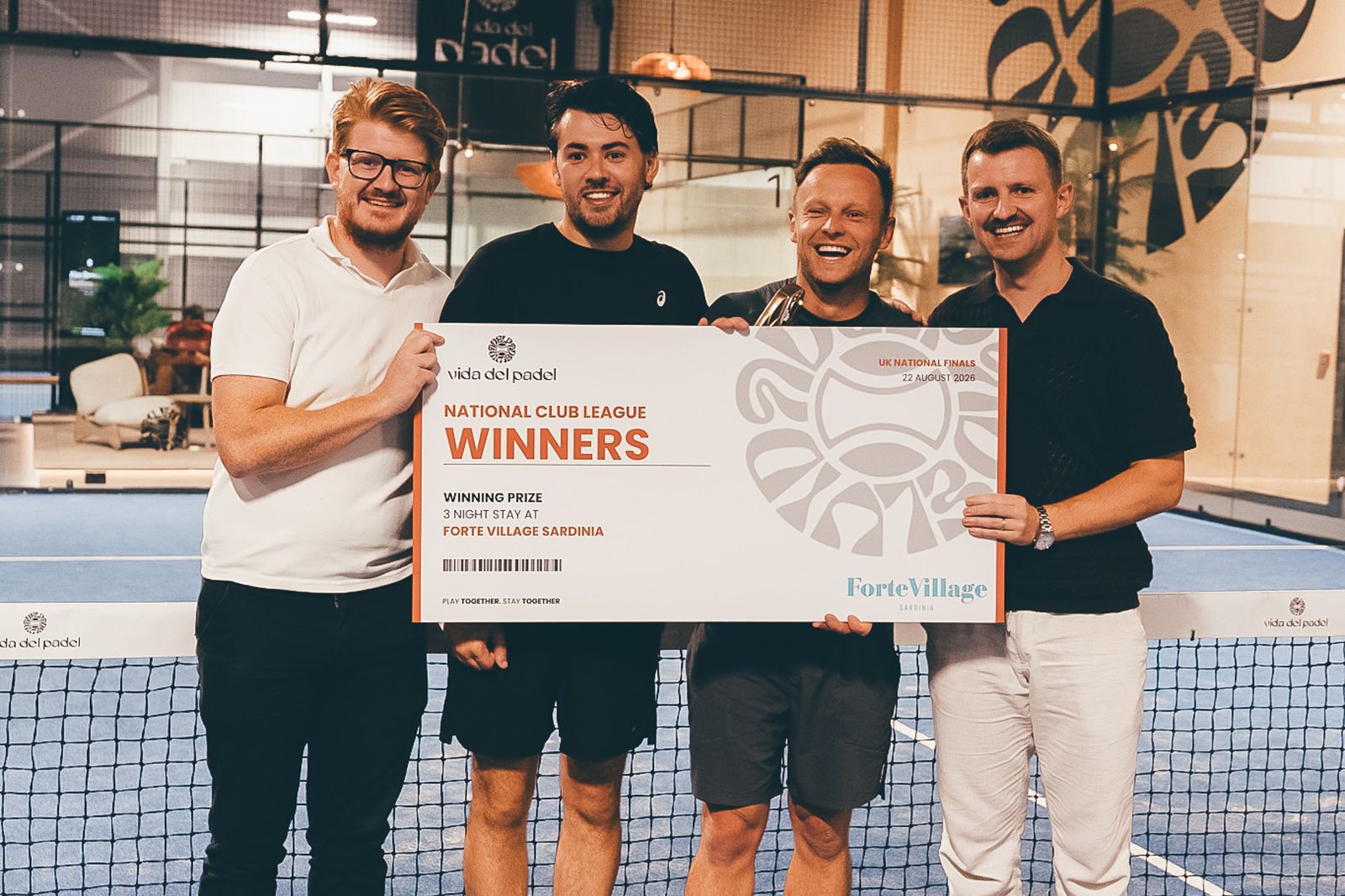 Four winners holding a large WINNERS cheque in front of a net at a Vida Del Padel final.